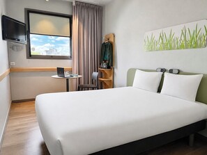 Habitación de hotel con una cama grande, un escritorio con una computadora portátil, un televisor y vista a la ciudad.