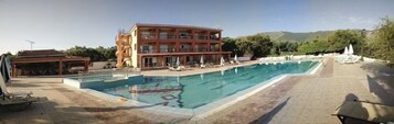 Un hotel con piscina, terraza con sillones y vistas a las montañas.