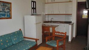 Un espacio habitable compacto con kitchenette, un sofá, una mesa de comedor y sillas de madera.