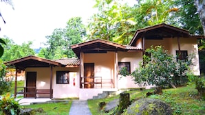 A bungalow with a porch, a pathway leading to the entrance, and a lush garden with trees and rocks. - Pousada Canto do Curió (Paraty)