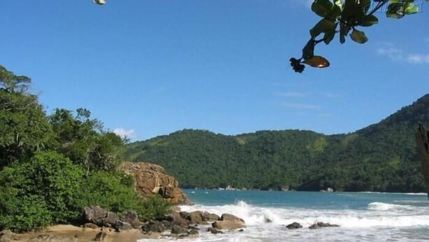 A beach with clear waters, rocky outcrops, and dense greenery. - Pousada Canto do Curió (Paraty)