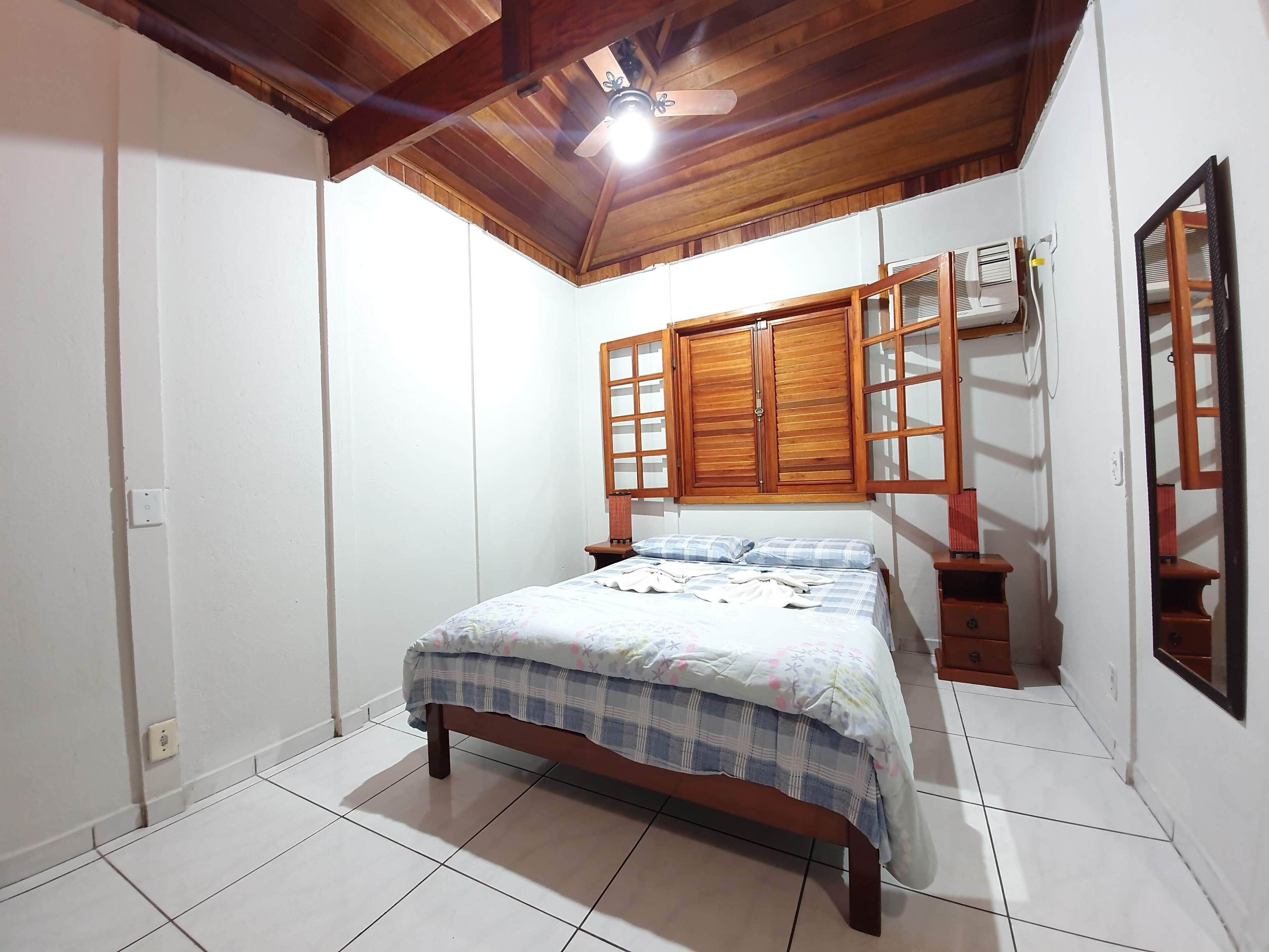 Un dormitorio con cama de madera, ventilador de techo y ventana con persianas de madera.