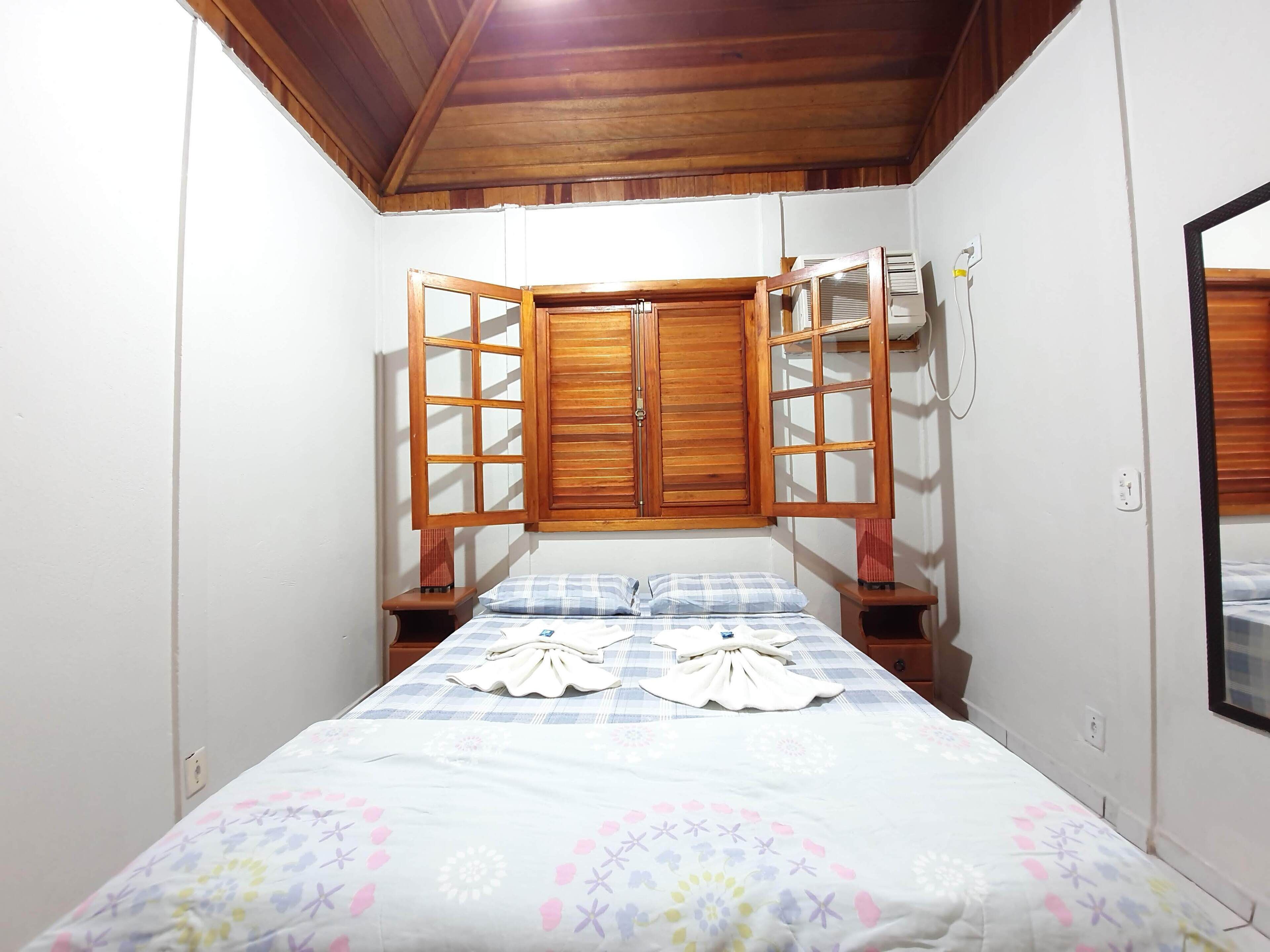 A bedroom with a bed, a wooden wardrobe, and a window with blinds.