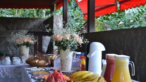 A table with food and drinks, including watermelon, bananas, and a pitcher of orange juice. - Pousada Canto do Curió (Paraty)