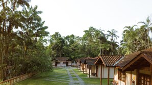 A row of traditional-style buildings with tiled roofs, arranged along a cobblestone pathway surrounded by lush greenery. - Pousada Canto do Curió (Paraty)