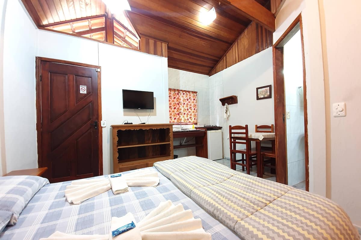 Quarto com cama, escrivaninha, televisão e uma pequena copa.