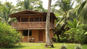 A two-story wooden house with a balcony, surrounded by lush greenery and palm trees. - Olguita s Place (Cahuita)