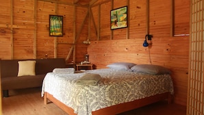 A wooden cabin room with a bed, a sofa, and two paintings on the walls. - Olguita s Place (Cahuita)