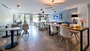 A modern dining area with multiple tables and chairs, a television mounted on the wall, and a large window providing natural light. - Appart'hôtel Kyriad Résidence Cabriès - Plan de Campagne (Cabries)