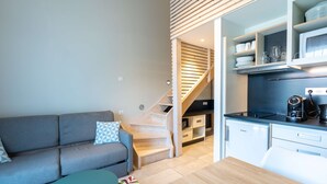 A compact living space with a sofa, a small table, a kitchen area with a microwave, and a staircase. - Appart'hôtel Kyriad Résidence Cabriès - Plan de Campagne (Cabries)