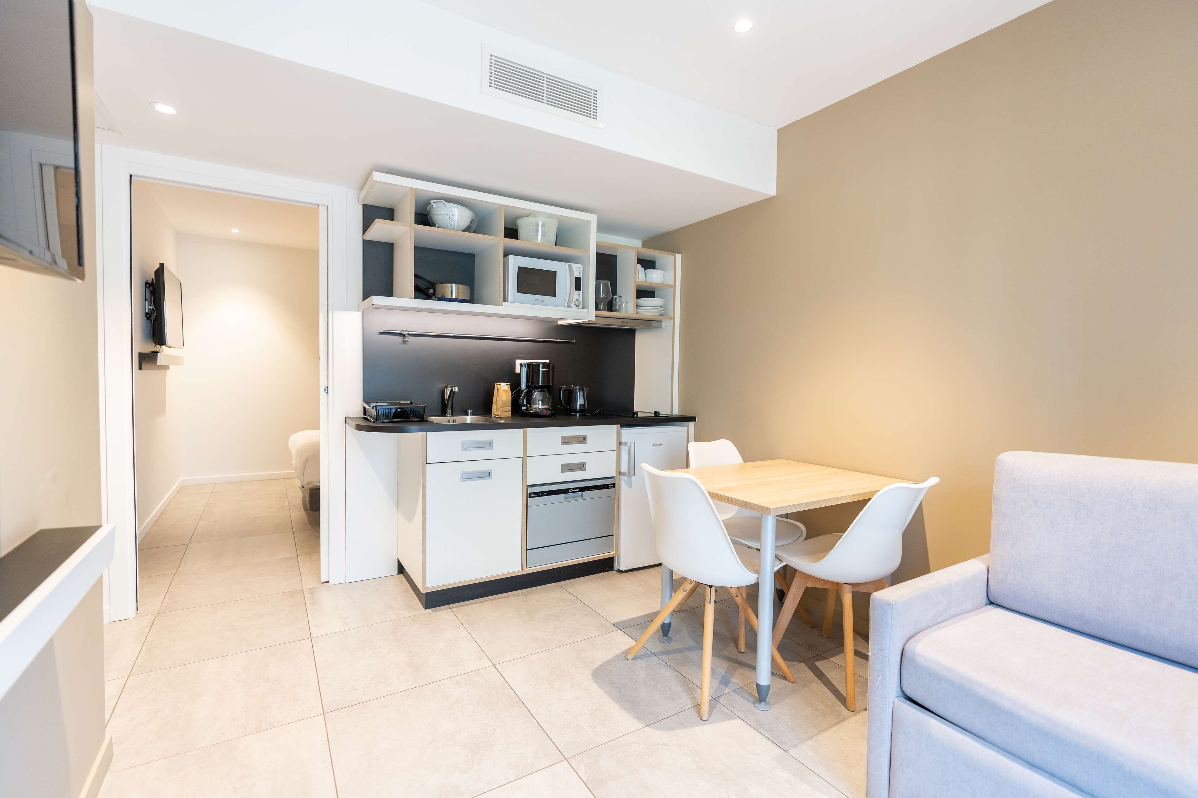 Una cocina moderna con armarios blancos, un microondas y una cafetera. Hay una mesa de comedor con dos sillas y un sofá.