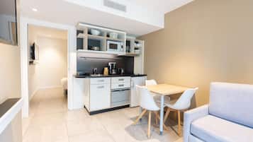 Una cocina moderna con armarios blancos, un microondas y una cafetera. Hay una mesa de comedor con dos sillas y un sofá.