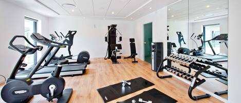 A modern gym with cardio machines, weight stations, and mirrors.