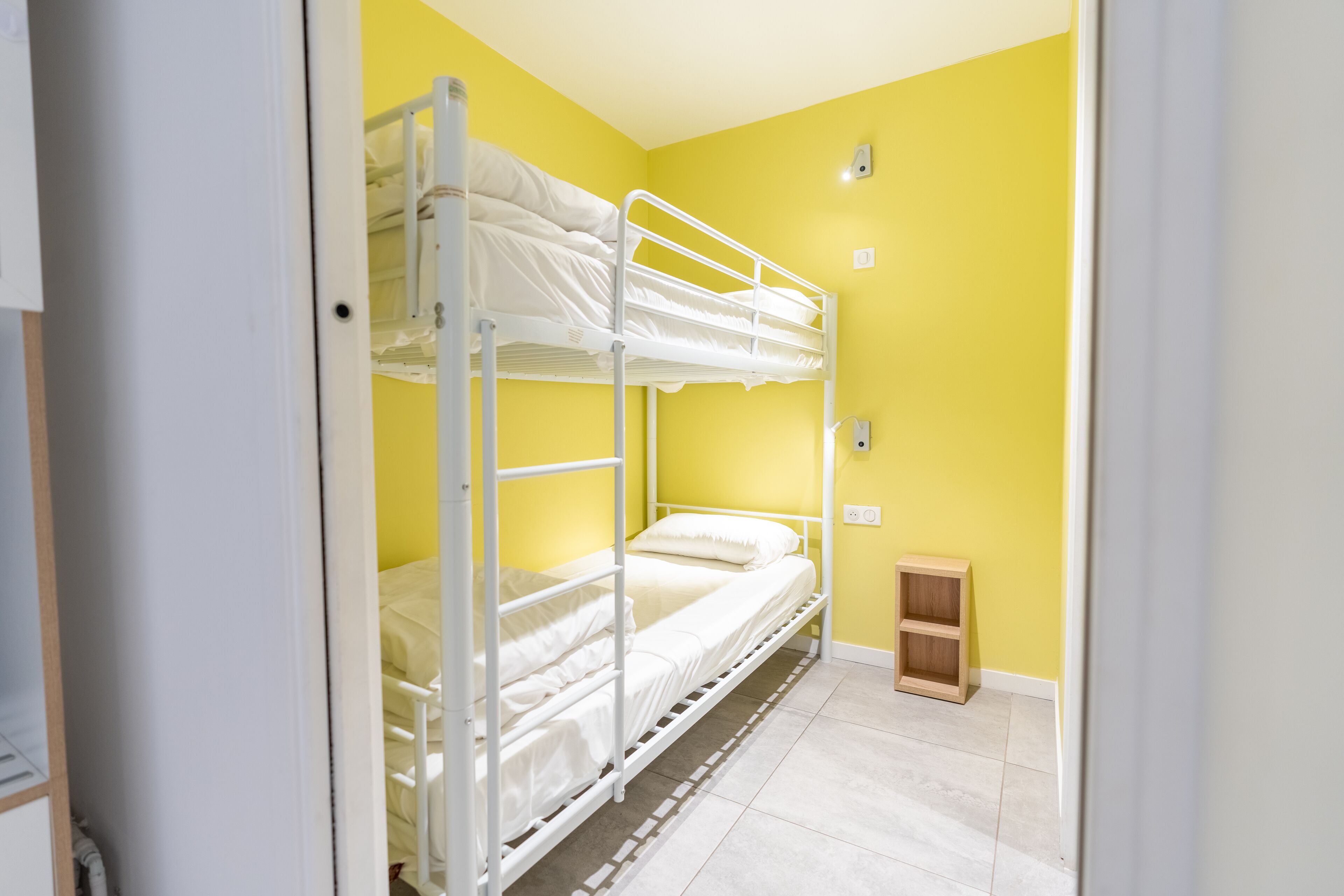 Una habitación con una cama litera, un pequeño armario de madera y un interruptor de luz en la pared.