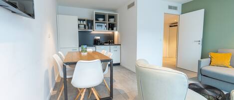 Una cocina moderna con armarios blancos, un microondas y una cafetera. Hay una mesa de comedor con sillas y un sofá en la zona de estar.