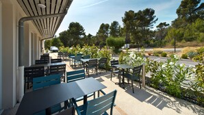 An outdoor patio with tables and chairs, surrounded by greenery and trees. - Appart'hôtel Kyriad Résidence Cabriès - Plan de Campagne (Cabries)