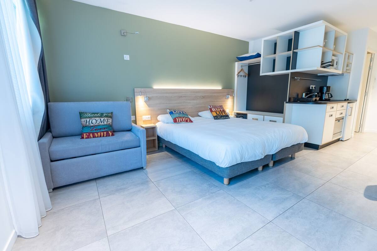 A modern bedroom with a bed, a sofa, a desk, and a kitchenette.