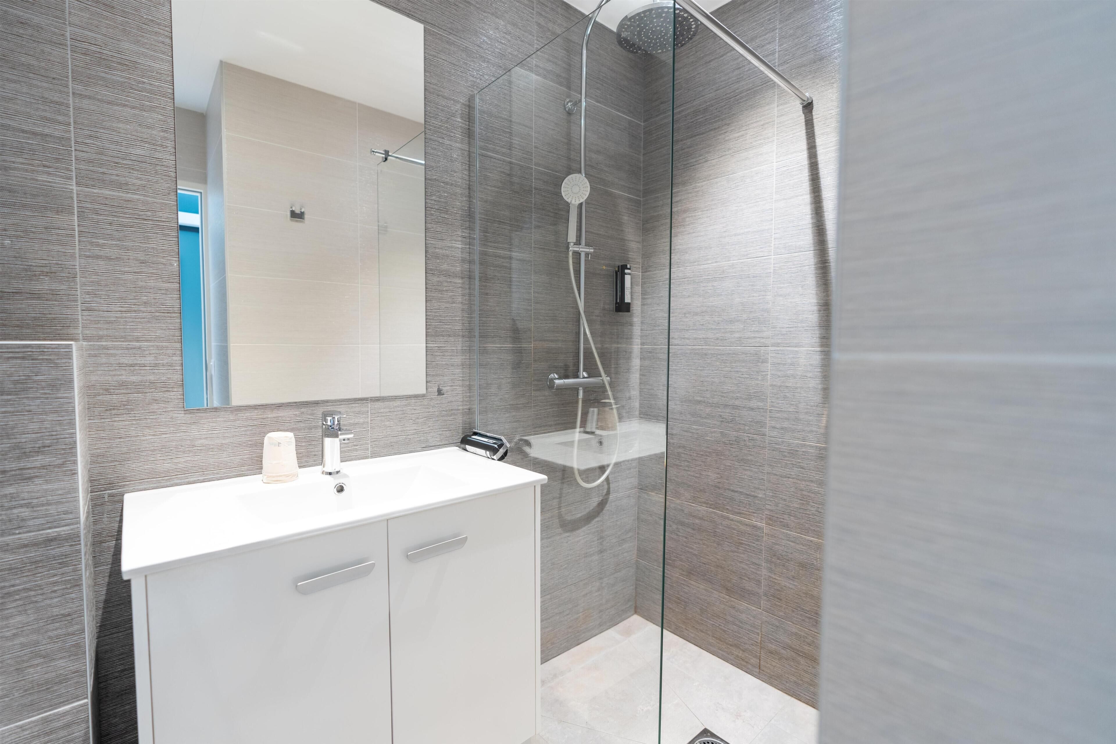 Un baño moderno con ducha de vidrio, tocador blanco y un espejo grande.