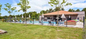 A pool area with lounge chairs and umbrellas, a covered seating area, and a building with a tiled roof. - Appart'hôtel Kyriad Résidence Cabriès - Plan de Campagne (Cabries)