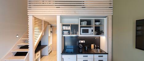 Cocina compacta con microondas, lavabo y armarios de almacenamiento. Se observa una pequeña mesa con sillas.