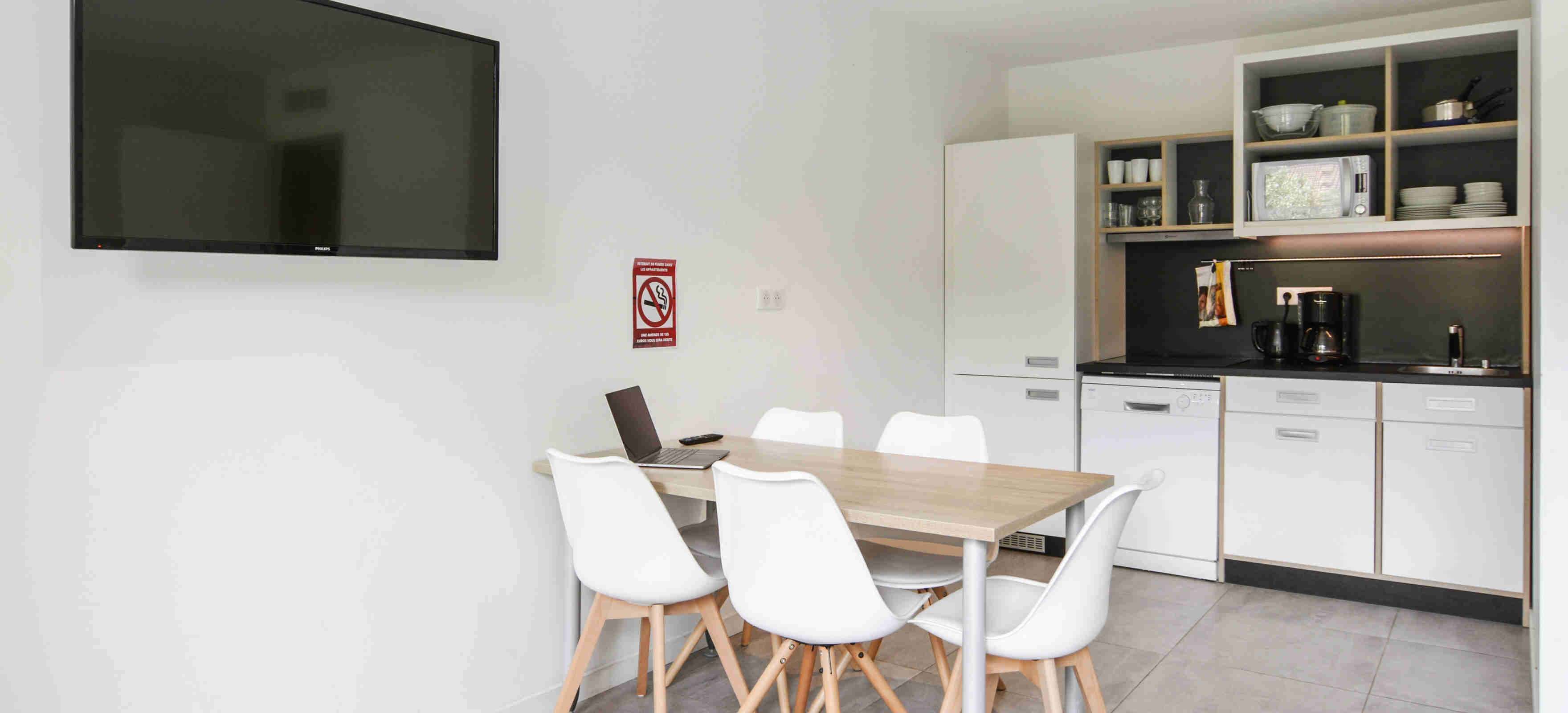 Une cuisine moderne avec des meubles blancs, un plan de travail noir et un coin repas comprenant une table en bois et des chaises blanches.