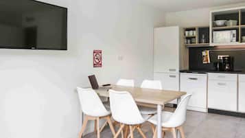 Eine moderne Küche mit weißen Schränken, einer schwarzen Arbeitsplatte und einem Essbereich mit Holztisch und weißen Stühlen.