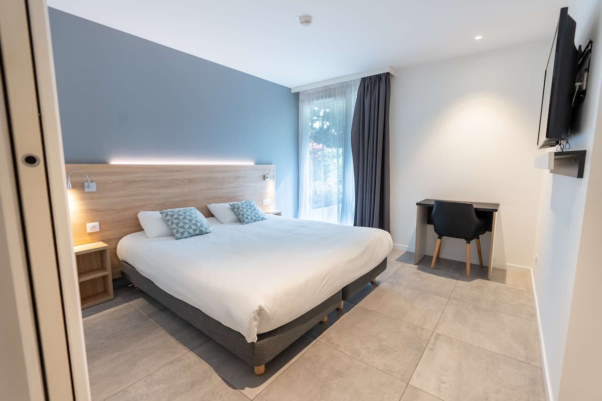 A modern bedroom with a large bed, bedside tables, a desk, and a TV.