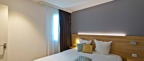 Ein modernes Hotelzimmer mit einem großen Bett, einem Holzkopfteil und einem Nachttisch mit einer Lampe.
