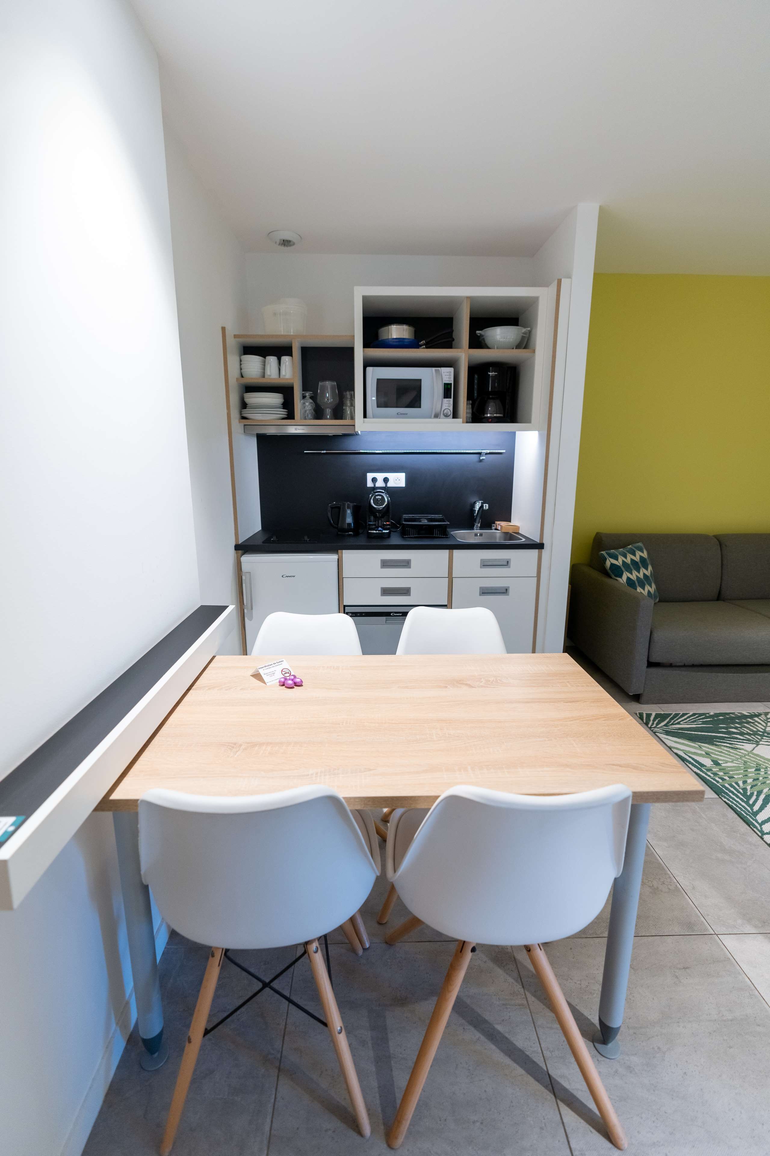 A compact kitchen with a dining table and chairs, a sofa, and a small refrigerator.