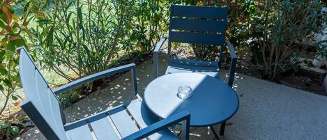 Un espace extérieur aménagé avec des sièges en métal bleu, comprenant une table et deux chaises, entouré de verdure et avec un bâtiment en arrière-plan.
