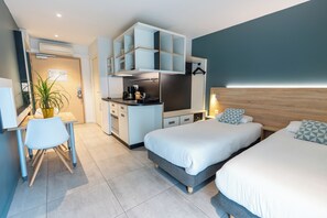A modern hotel room with a kitchenette, two beds, a desk, and a potted plant. - Appart'hôtel Kyriad Résidence Cabriès - Plan de Campagne (Cabries)