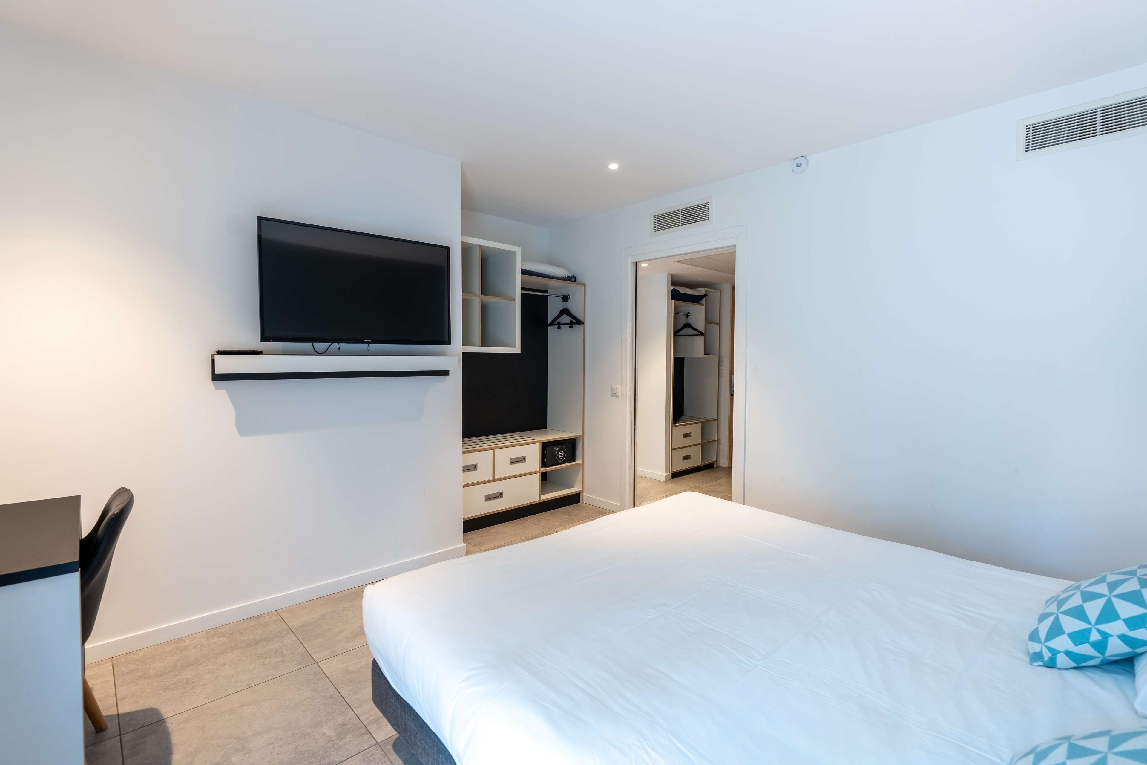 Een moderne slaapkamer met een bed, een aan de muur bevestigde televisie, een bureau en een inloopkast.