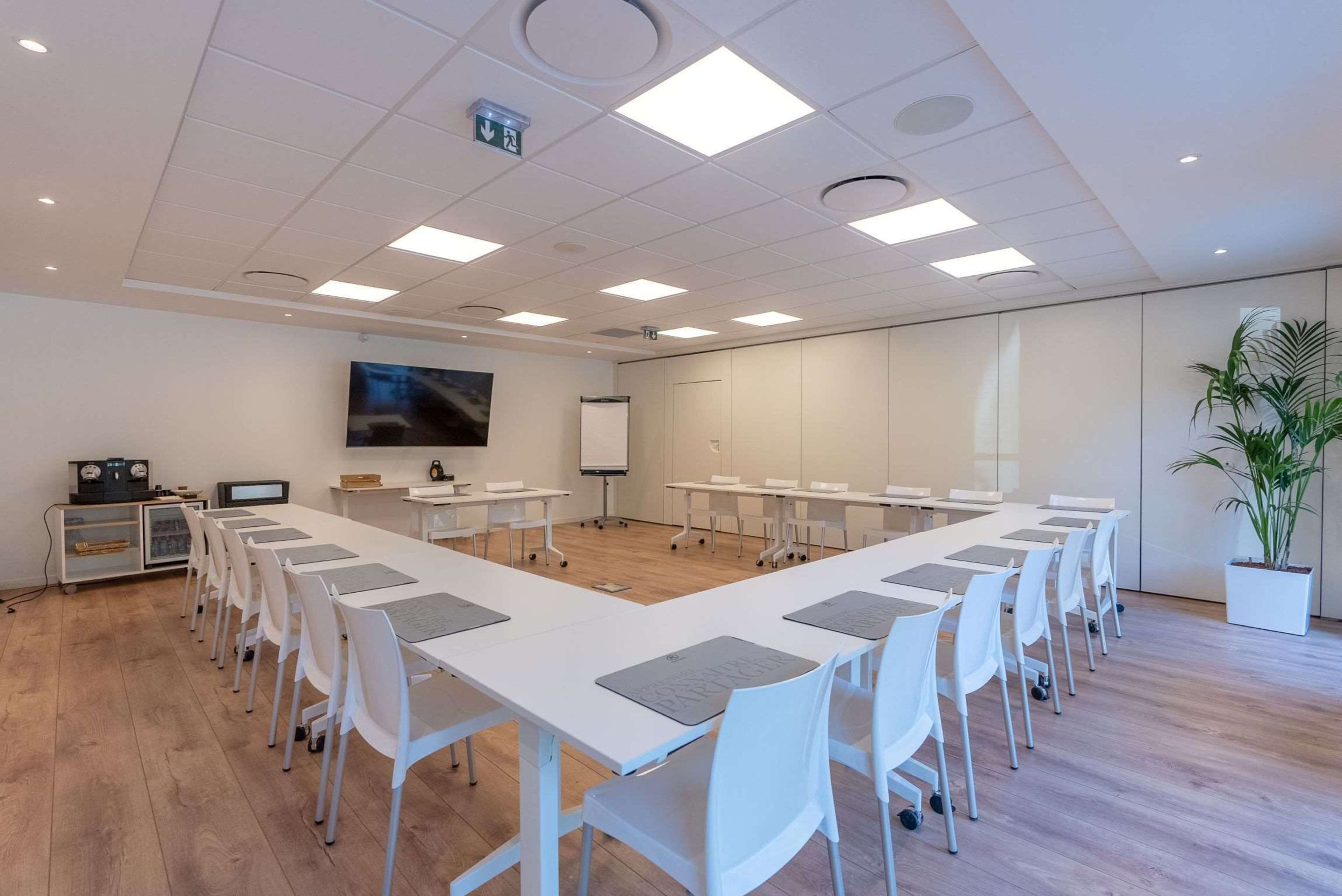 A conference room with white tables and chairs, a large screen, and a whiteboard.