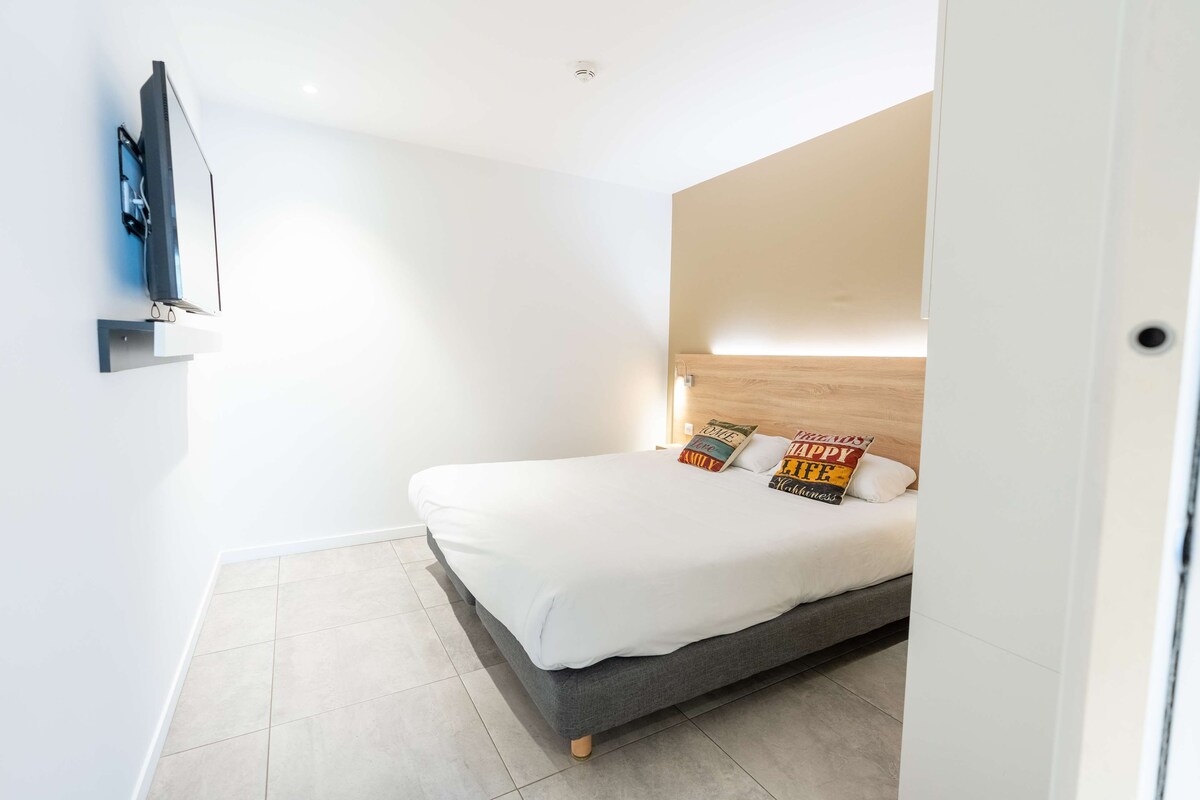 A modern bedroom with a bed, a mounted TV, and a wooden headboard.