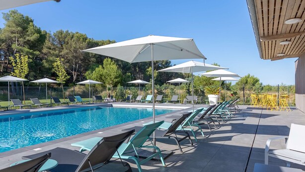 A poolside area with lounge chairs and umbrellas, a clear blue sky, and trees in the background. - Appart'hôtel Kyriad Résidence Cabriès - Plan de Campagne (Cabries)