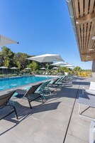 Una piscina al aire libre, sombrillas, sillones reclinables de piscina