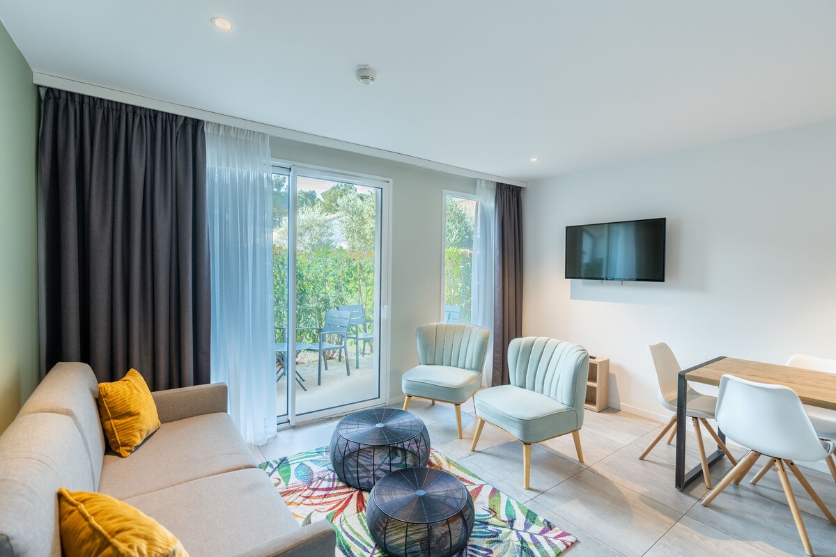 A modern living room with a sofa, chairs, a dining table, and a TV mounted on the wall.