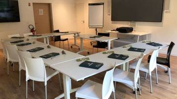Sala de conferências com mesas brancas, cadeiras, projetor e tela.