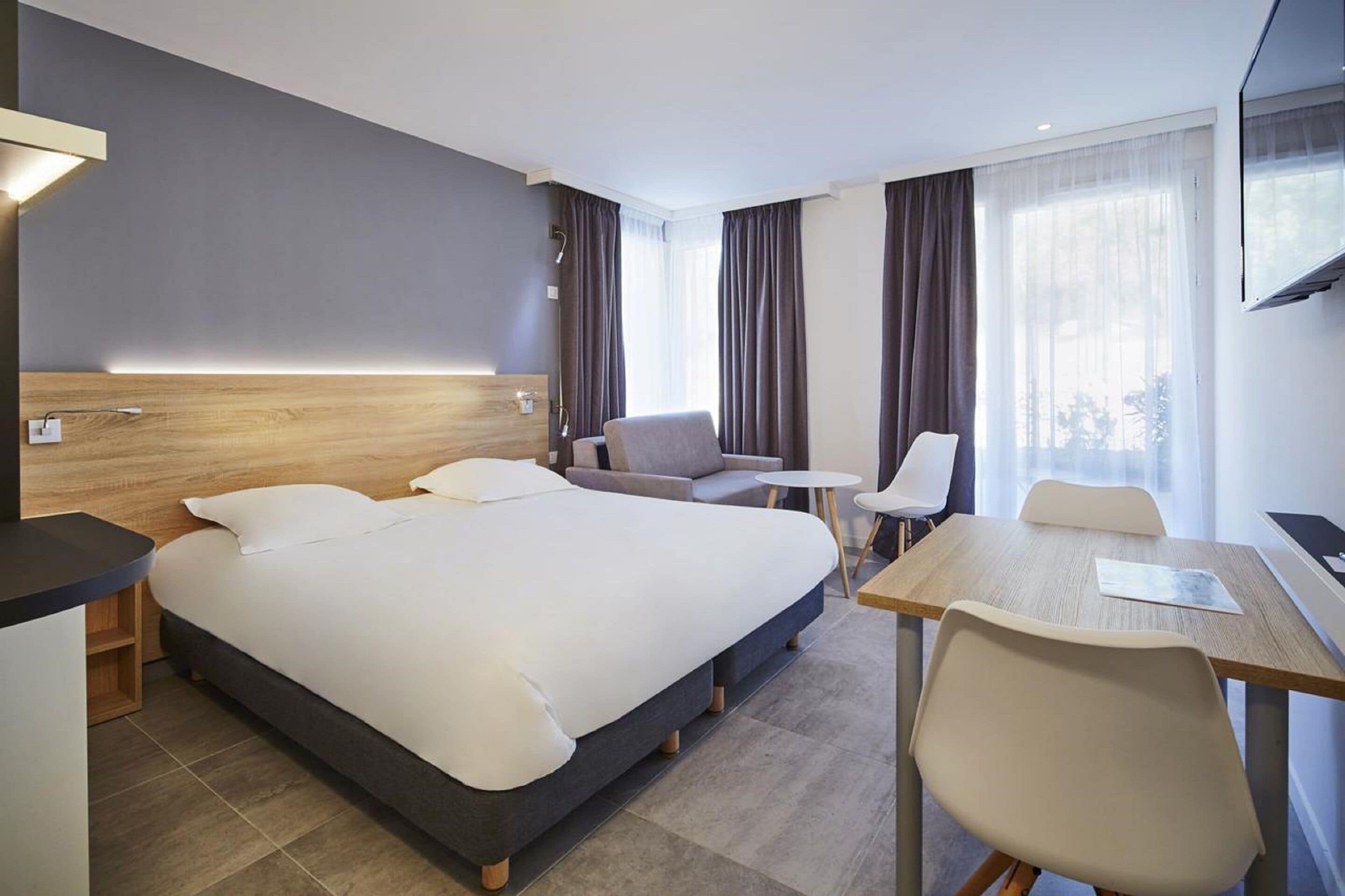 A modern hotel room with a large bed, a desk, a chair, and a TV.