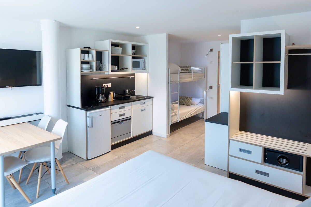 A modern, compact room with a bunk bed, kitchenette, and a flat-screen TV.
