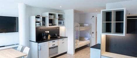 A modern, compact room with a bunk bed, kitchenette, and a flat-screen TV.