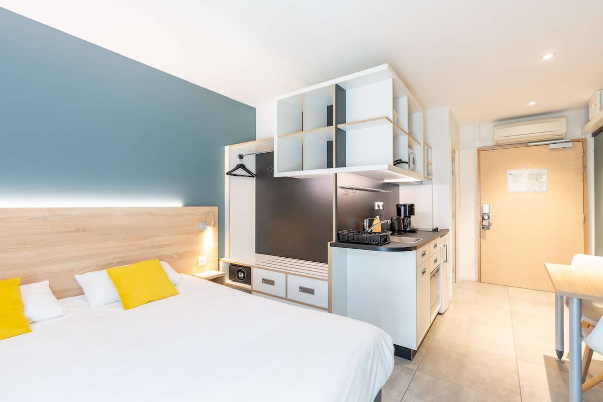 A modern hotel room with a bed, a kitchenette, and a separate dining area.