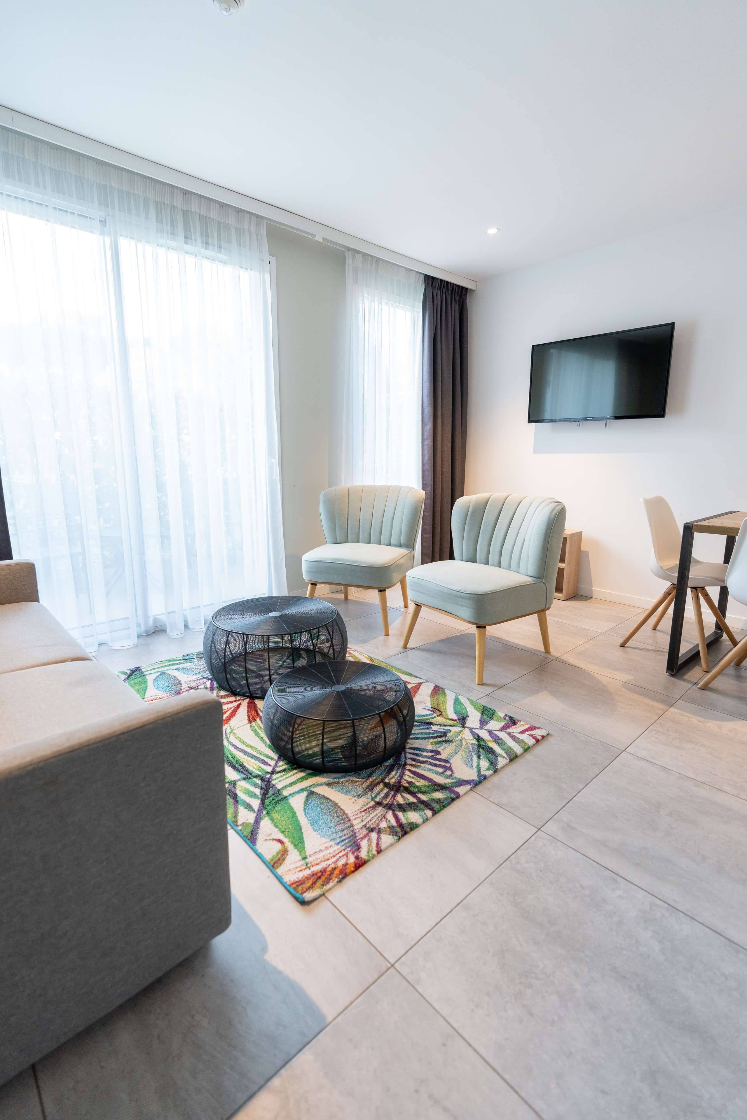 Uma sala de estar moderna com um sofá, duas poltronas, uma mesa de centro e uma TV fixada na parede.