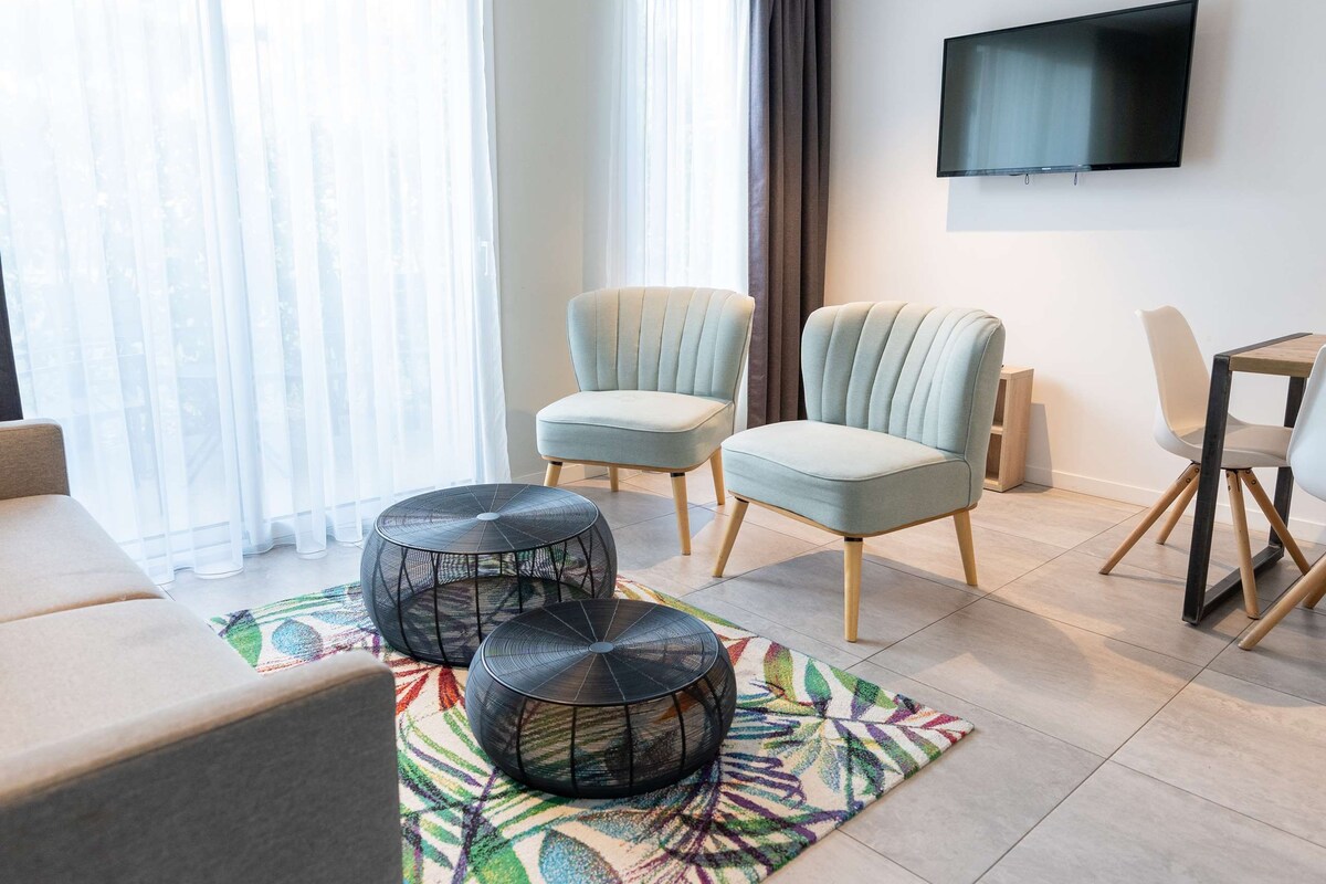 A modern living room with a sofa, two armchairs, a coffee table, and a TV mounted on the wall.