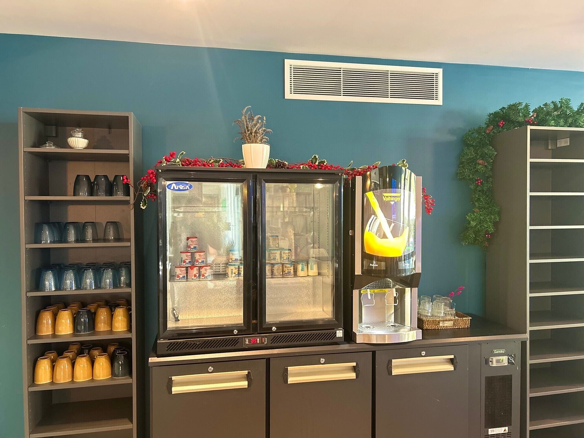Un espace dédié aux boissons, comprenant une machine à café, un réfrigérateur-vitrine et des étagères avec des bocaux.