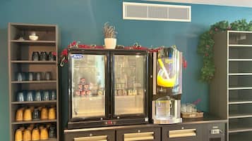 Un espace dédié aux boissons, comprenant une machine à café, un réfrigérateur-vitrine et des étagères avec des bocaux.