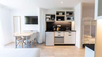 Una kitchenette moderna y compacta con microondas, horno y cafetera integrados. Cuenta con un pequeño comedor con mesa y sillas, y un televisor montado en la pared.