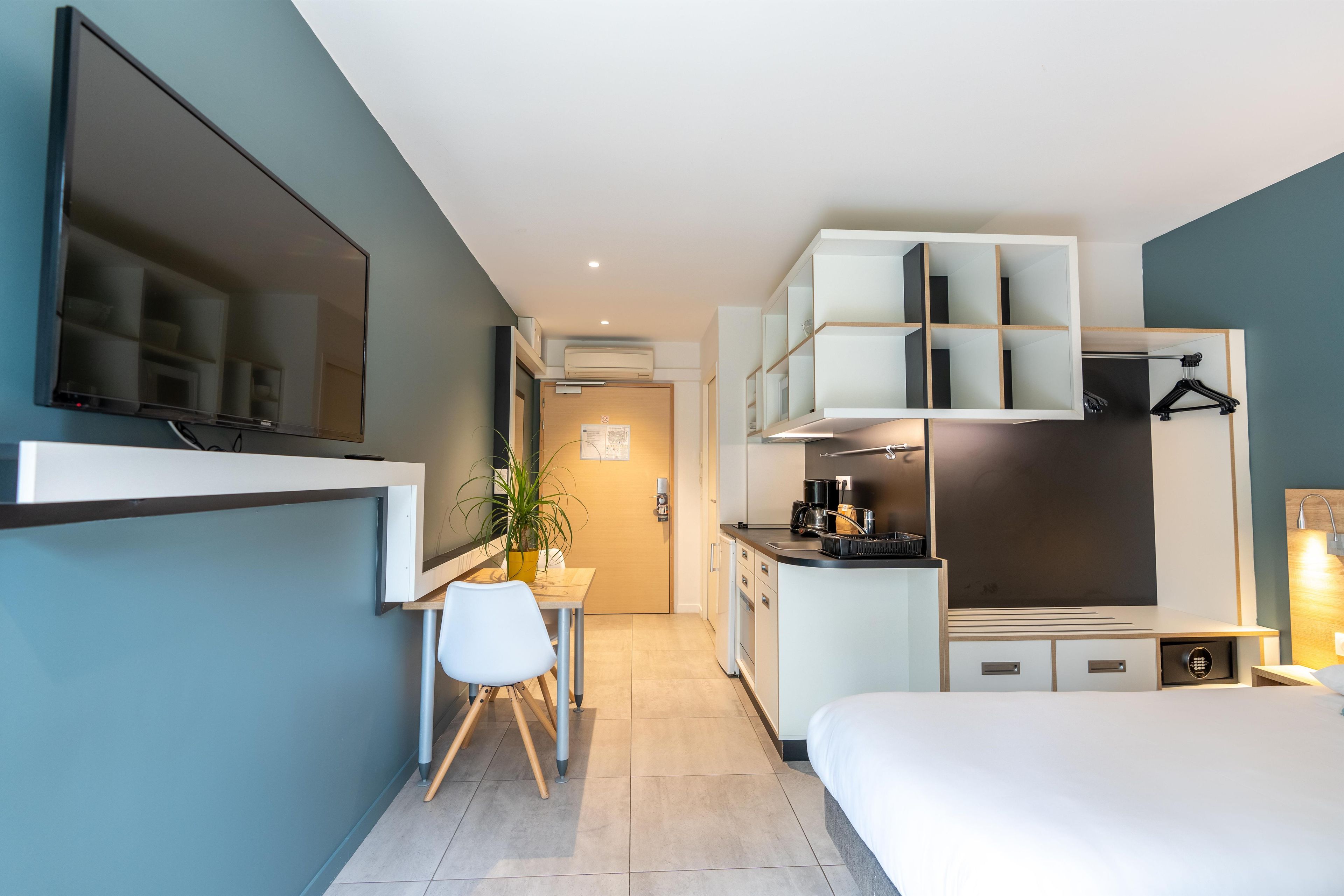 Een moderne hotelkamer met een bed, bureau, stoel, televisie, kitchenette en badkamer.