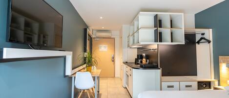 A modern hotel room with a bed, a desk, a chair, a TV, a kitchenette, and a bathroom.