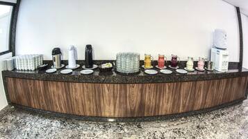 Una encimera de cocina con diversos electrodomésticos y objetos, incluyendo una cafetera, un hervidor y platos apilados.